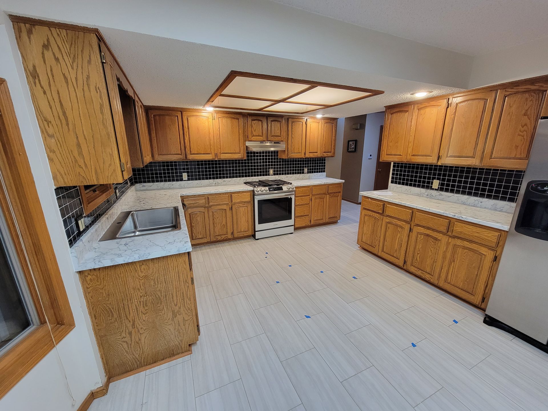 Kitchen with light wood cabinets, white countertops, black backsplash, and light wood flooring.