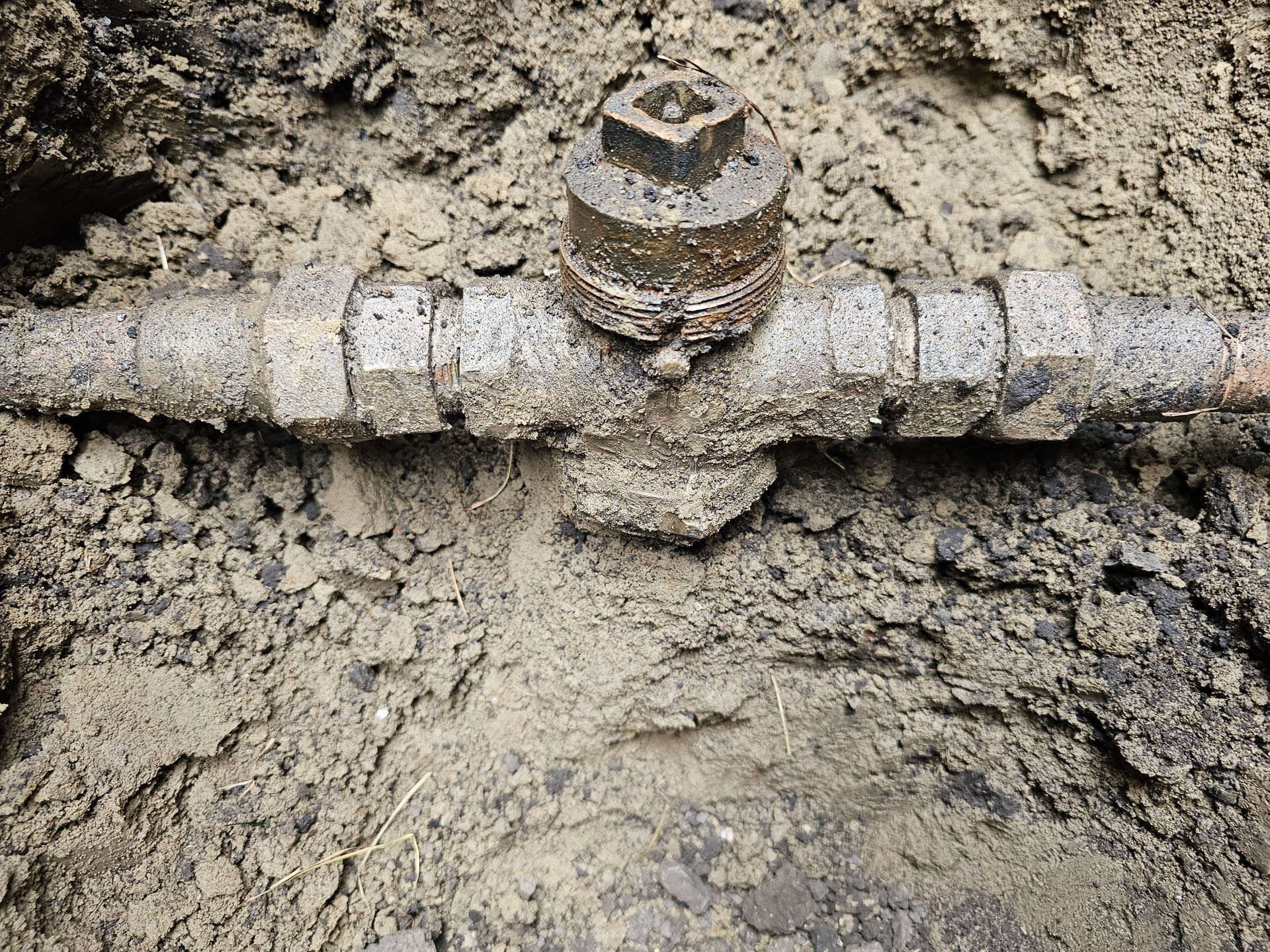 Metal pipe and valve buried in dirt.