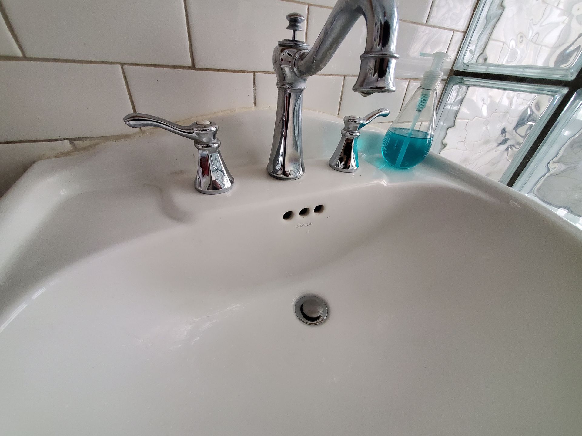 White bathroom sink with chrome faucet and handles, a blue liquid soap bottle sits on the right.
