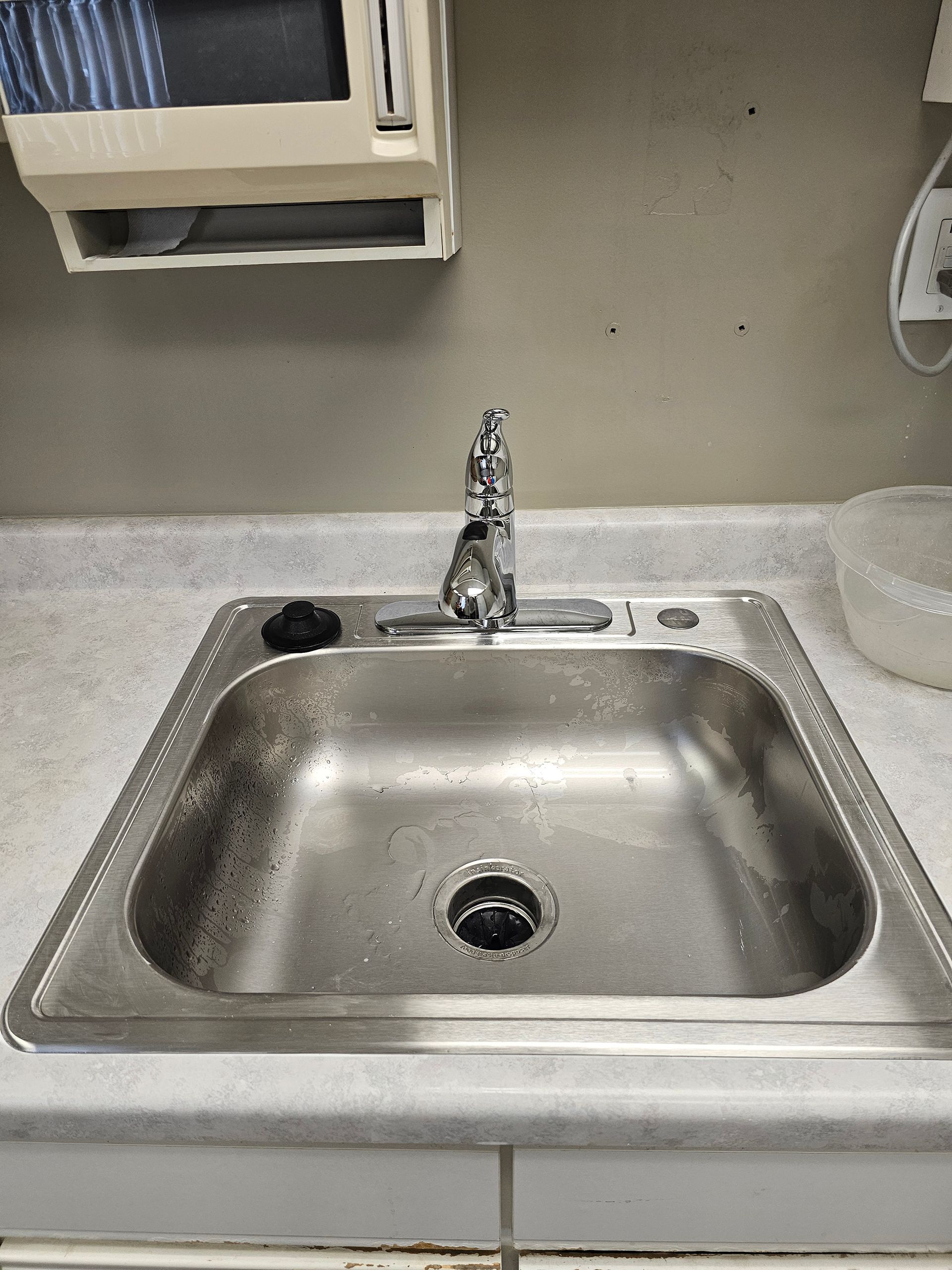 Stainless steel sink with faucet, mounted on countertop, with paper towel dispenser above.
