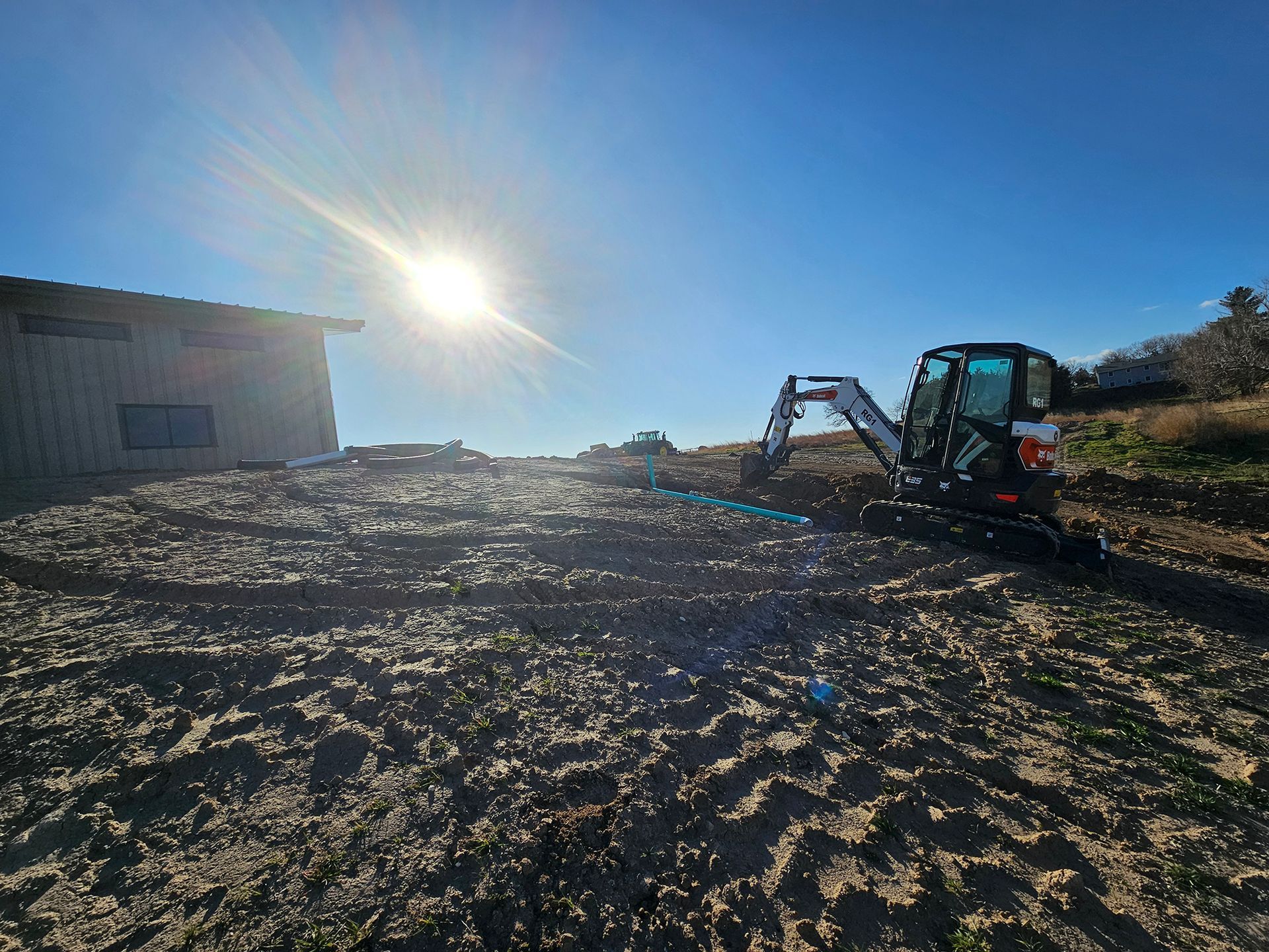 Bobcat excavator on a construction site clearing land under a bright sun.