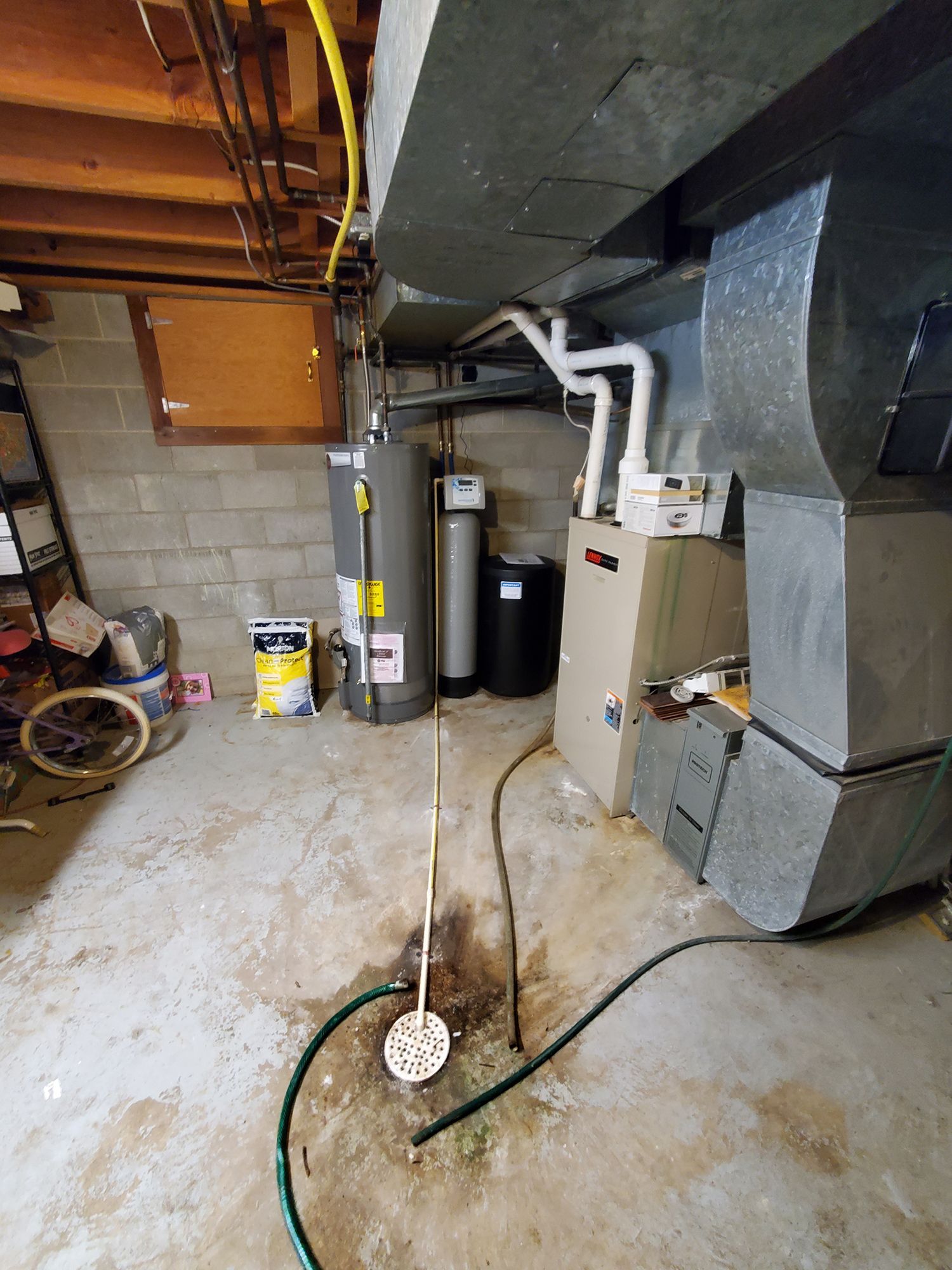 Basement interior with water heater, furnace, and water softener. Wet floor with a sump pump and hose visible.