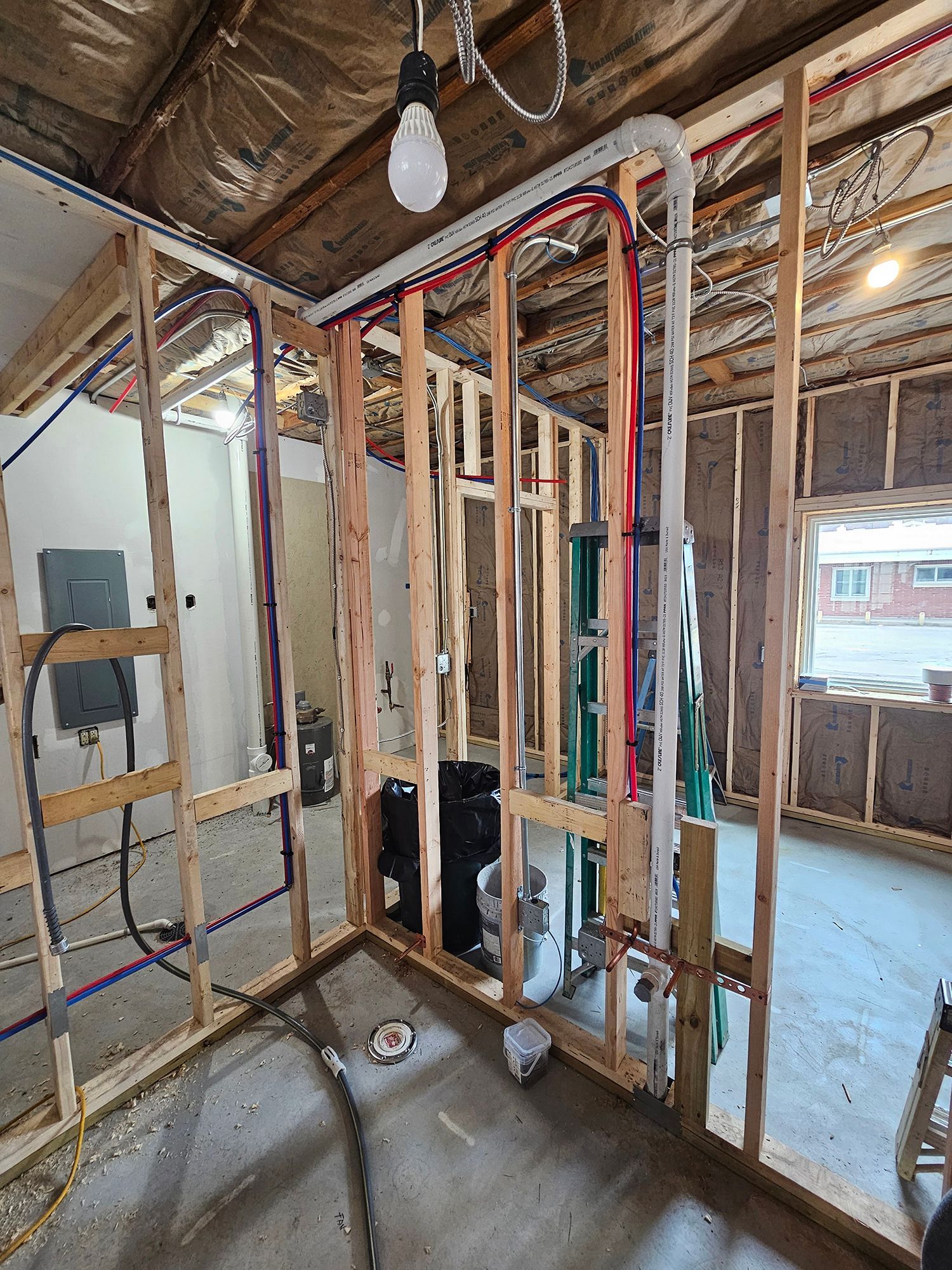 Framed interior room under construction with exposed plumbing and electrical wiring.