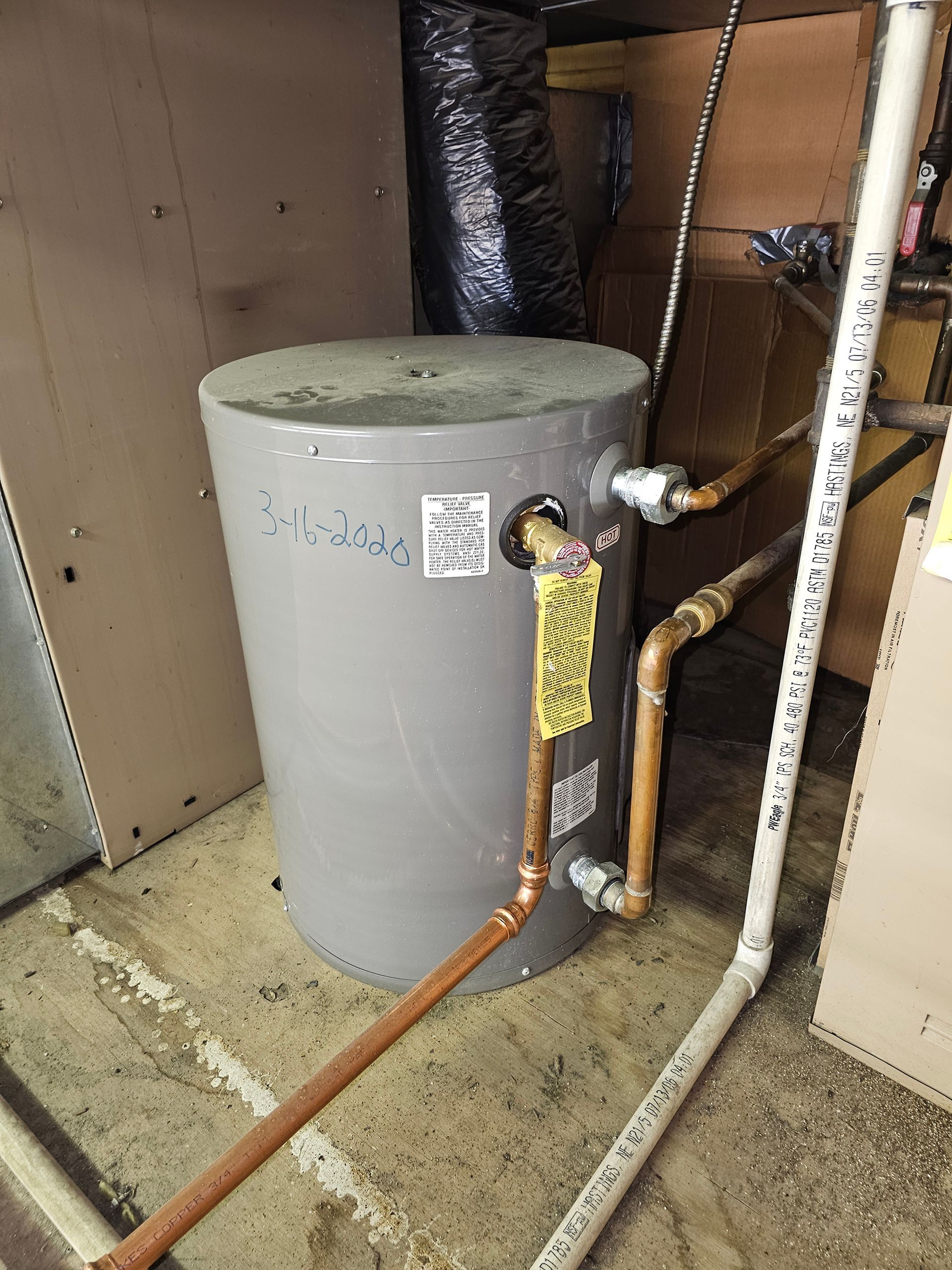 Gray water heater with copper and white pipes in a utility room.