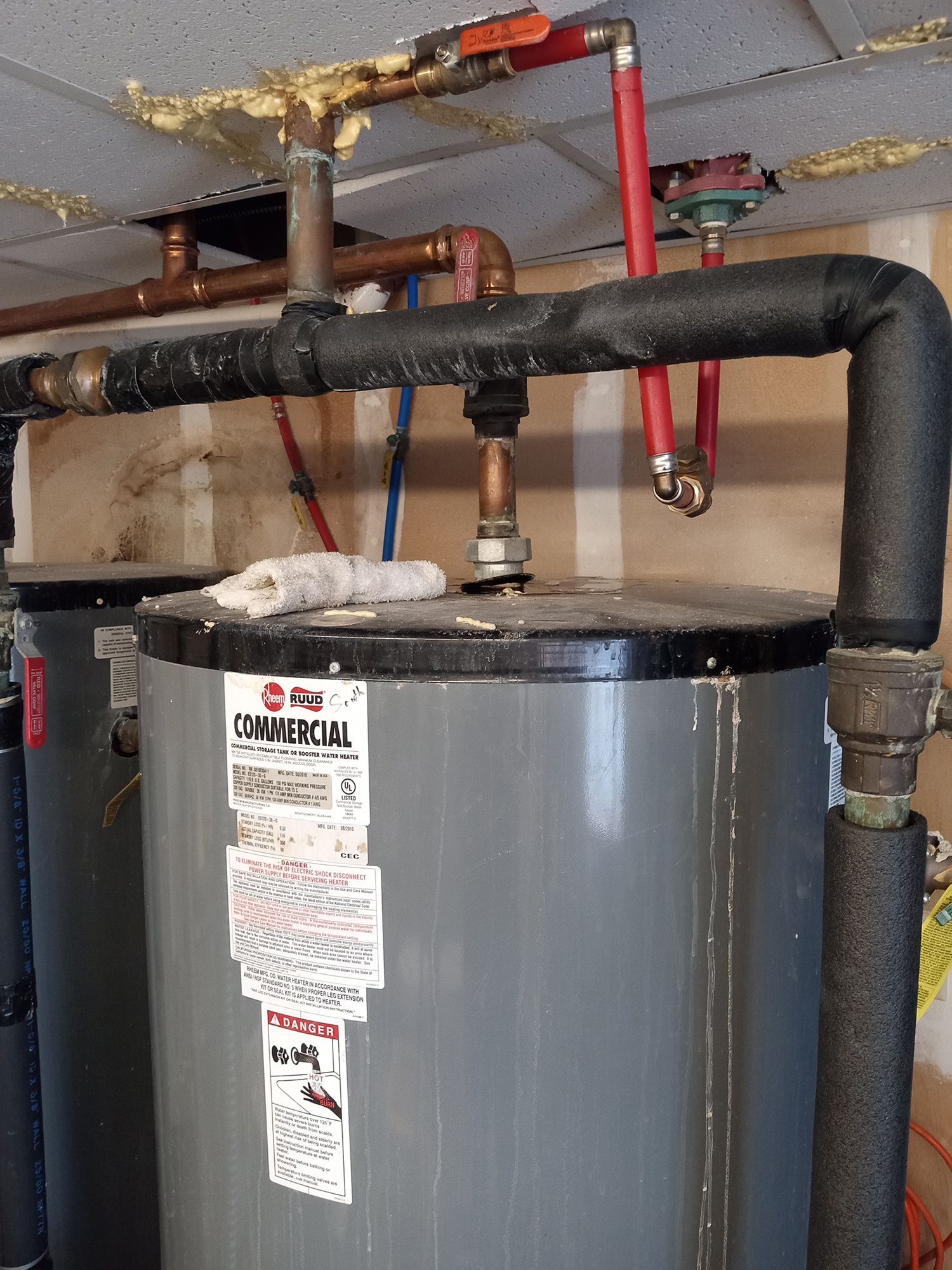 Two gray water heaters with connected pipes and insulation in a utility room.