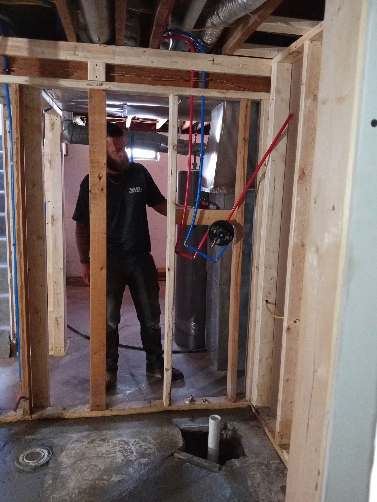 Man in unfinished room with exposed plumbing. Framing is visible, blue and red pipes.