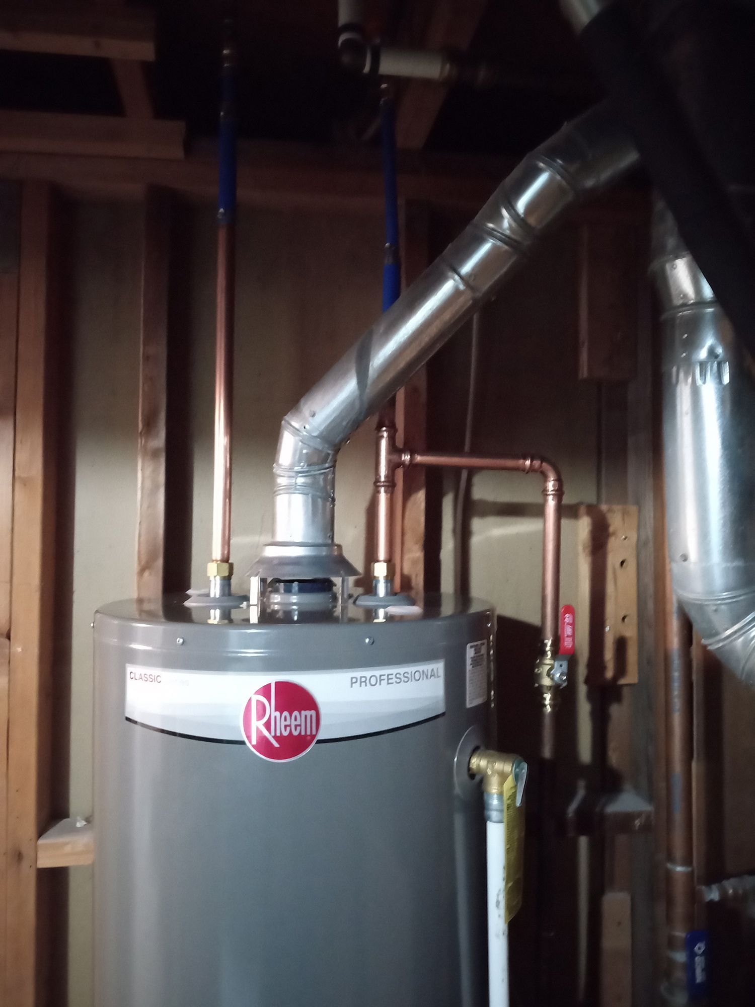 A water heater with copper pipes and a metal vent in a wooden-framed utility room.