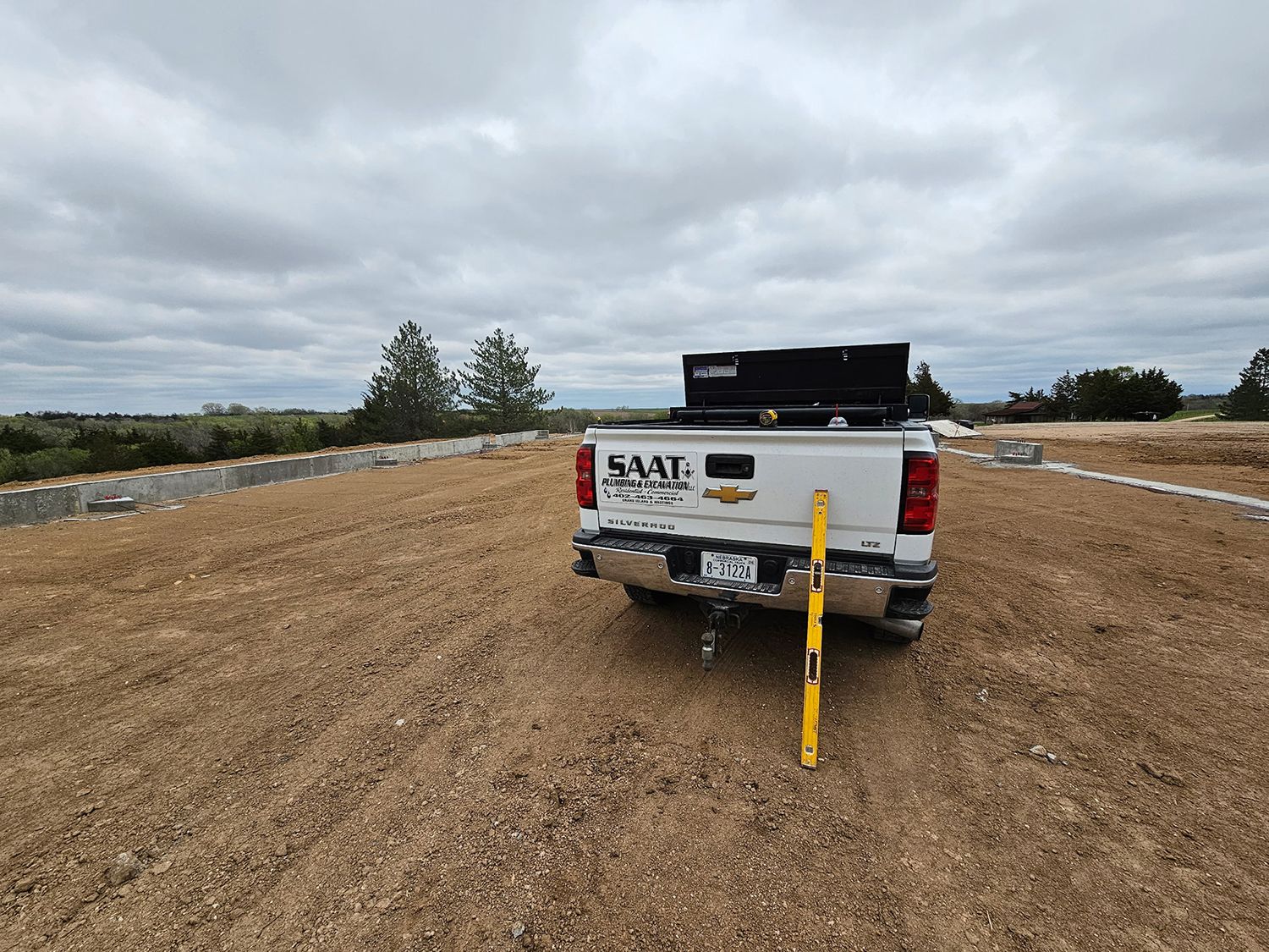 Truck parked on gravel at a construction site, with a level leaning against the bumper under a cloudy sky.