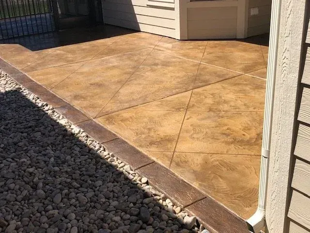 Brown stained concrete patio with geometric design, brown border, and gravel landscaping.