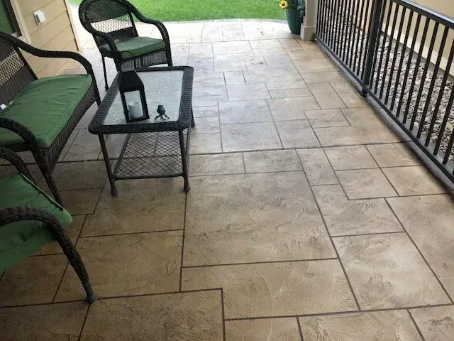 Patio with stamped concrete flooring, wrought iron furniture with green cushions, and a black railing.