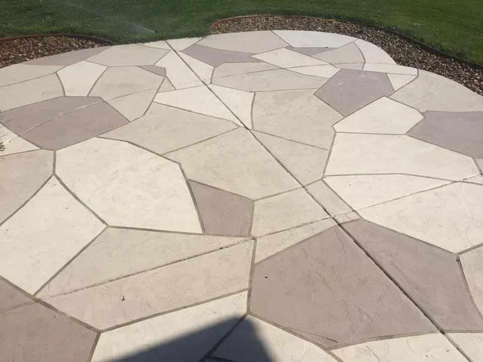 Tiled patio with various light and dark gray geometric shapes. The patio is surrounded by grass and dark mulch.