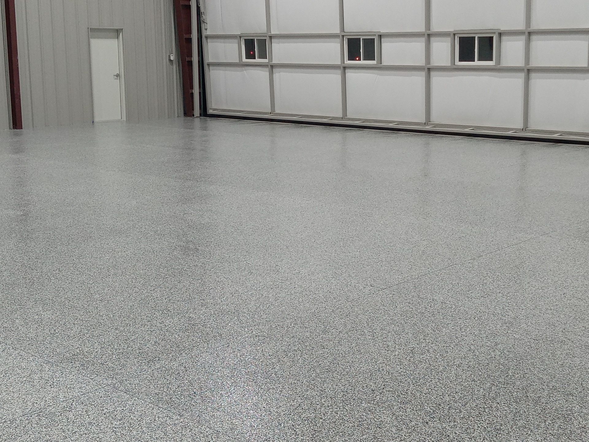 Gray speckled epoxy floor in a warehouse, with a white wall, door, and windows.