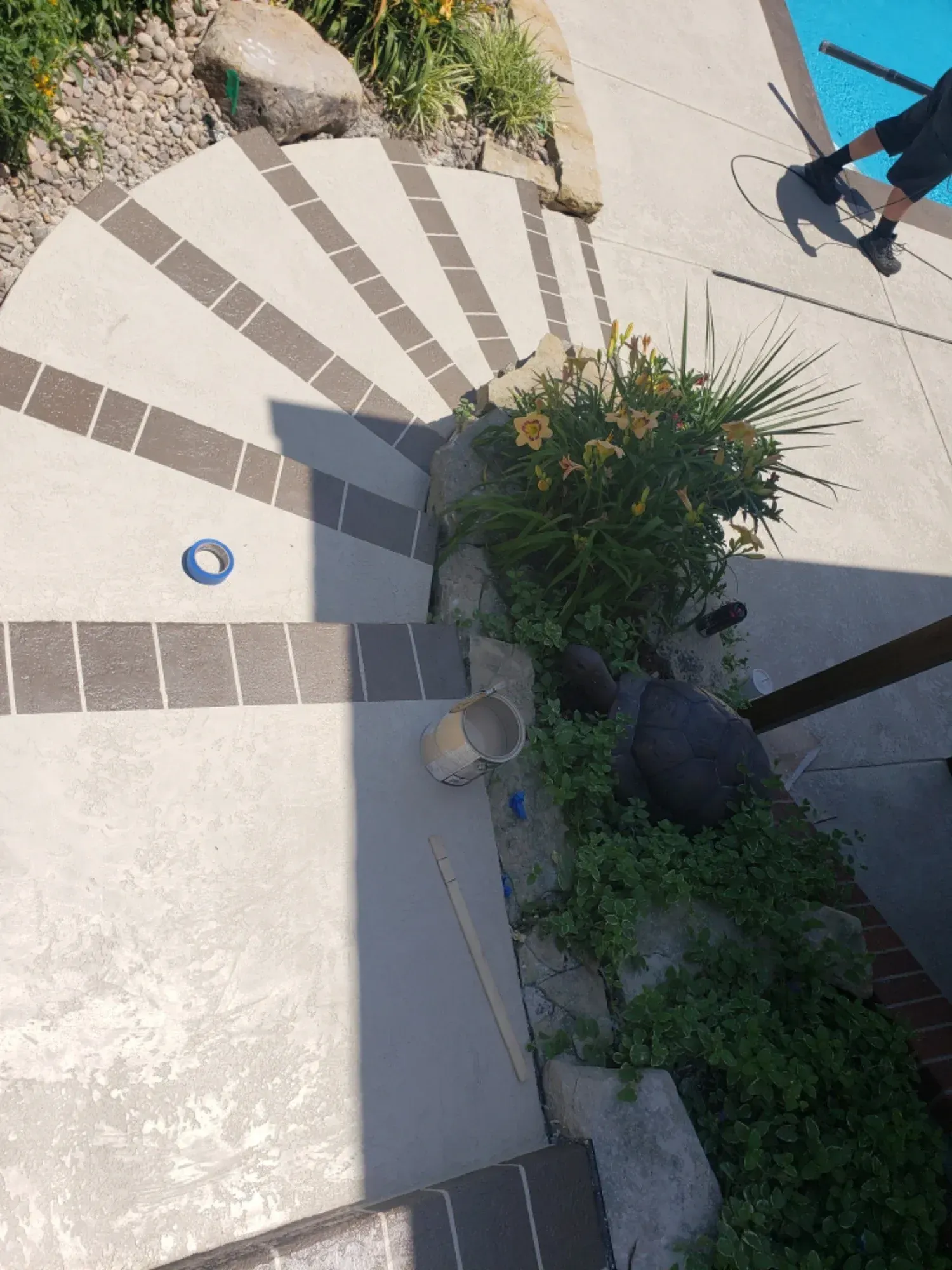 Curved concrete steps with dark border, leading down.  Plants and rocks in the corner. Person on the right.