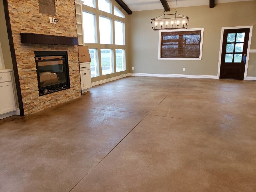 Living room with a stone fireplace, large windows, and brown stained concrete floor.