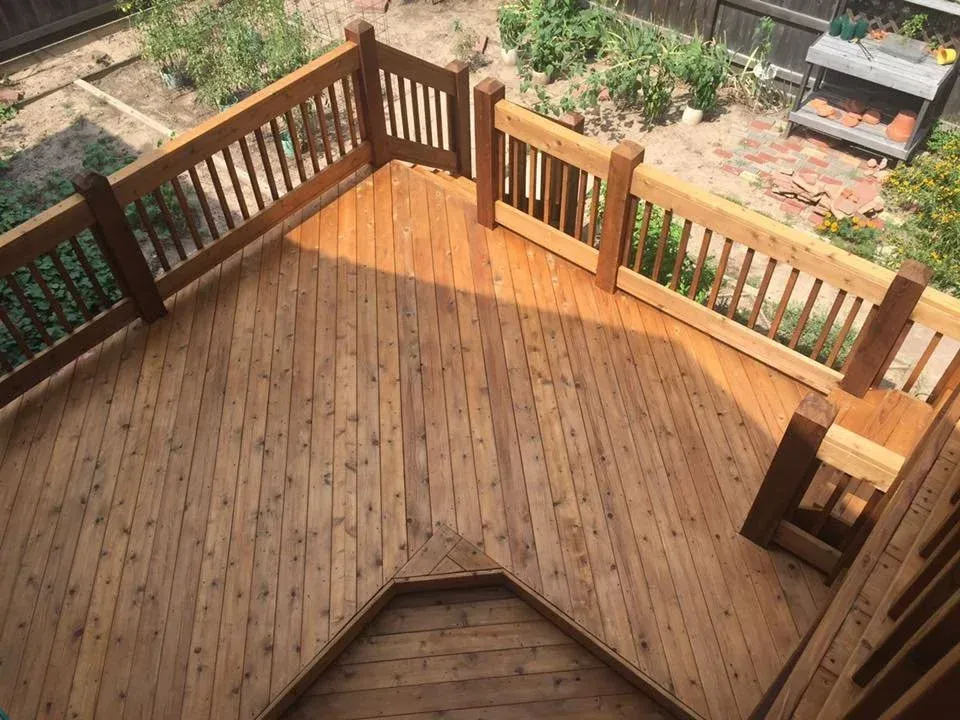 Wooden deck with railings, viewed from above, surrounded by a garden.