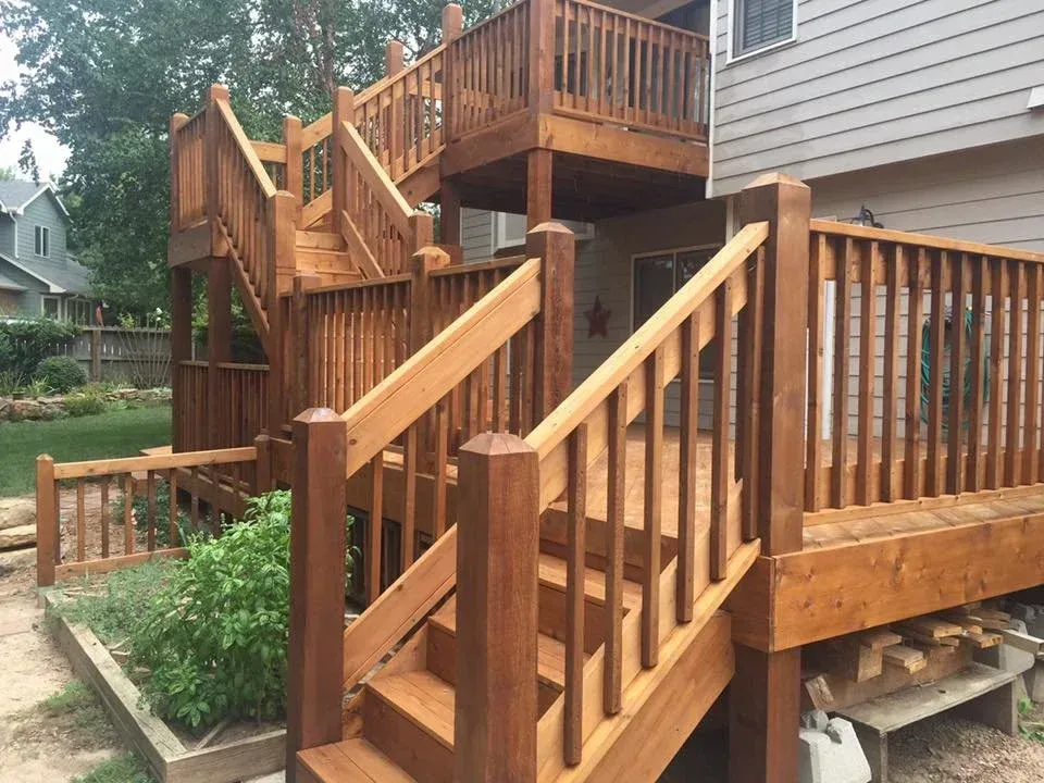 Wooden multi-level deck with stairs stained brown, connecting to a house.