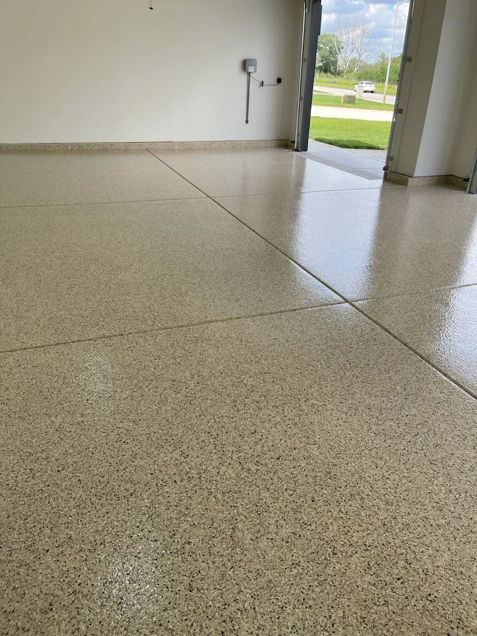Epoxy-coated garage floor with tan and black flecks, reflecting light. Open garage door, white walls.