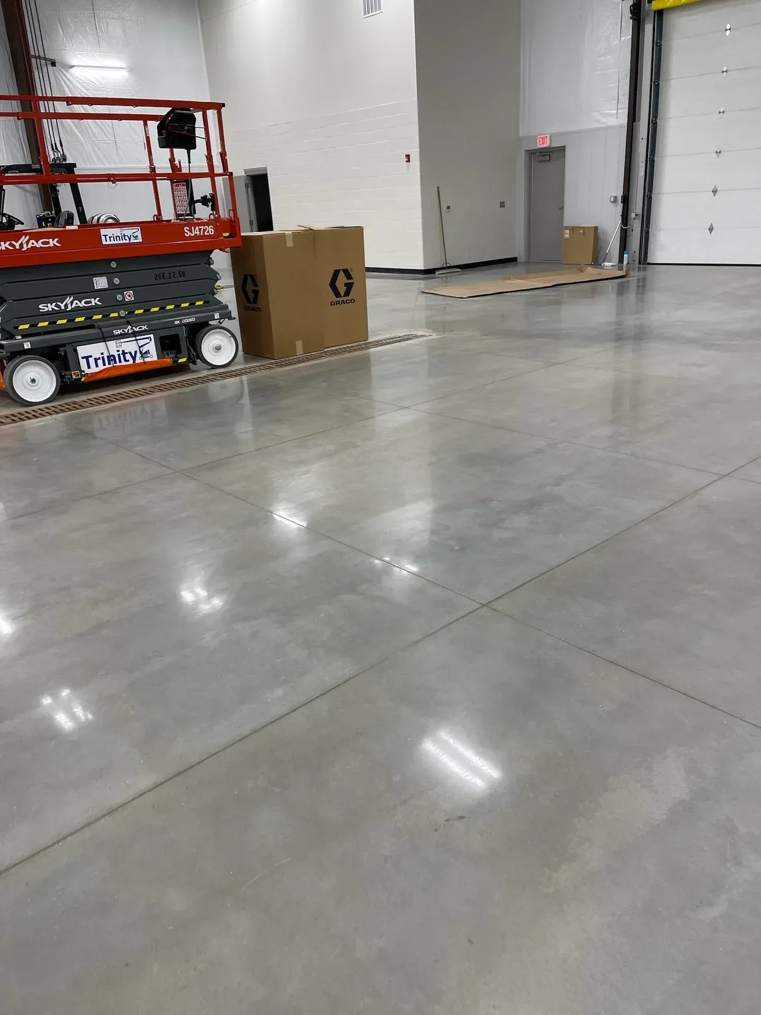 Warehouse interior with shiny concrete floor. Red lift equipment. Cardboard boxes near a closed garage door.