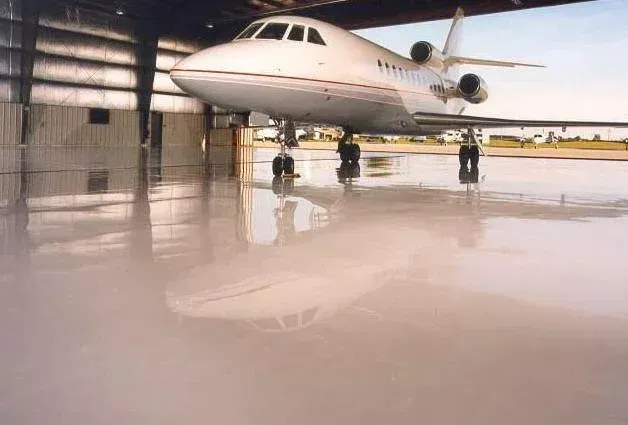Private jet in a hangar, reflected in a shiny, smooth, light gray floor.