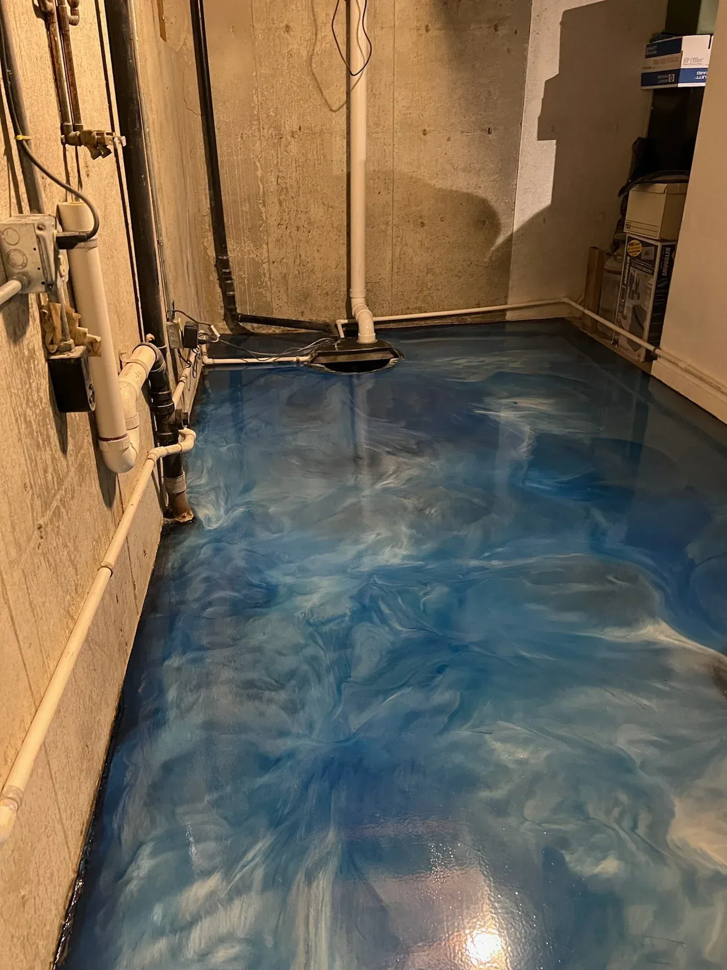 Basement with blue and white swirled epoxy floor. Concrete walls and pipes visible.