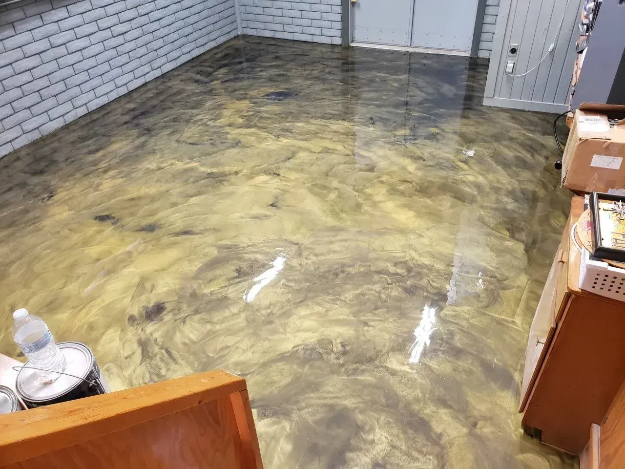 Metallic gold and black epoxy flooring in a room, with a brick wall and partially visible wooden cabinets.