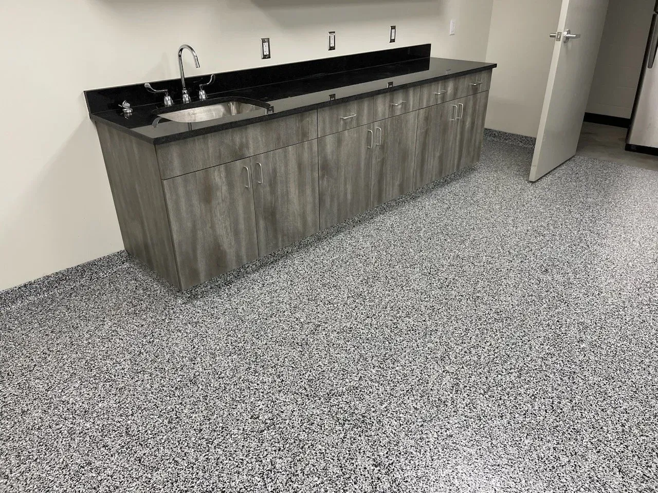 Gray speckled epoxy floor with a gray wood cabinet and black countertop sink.