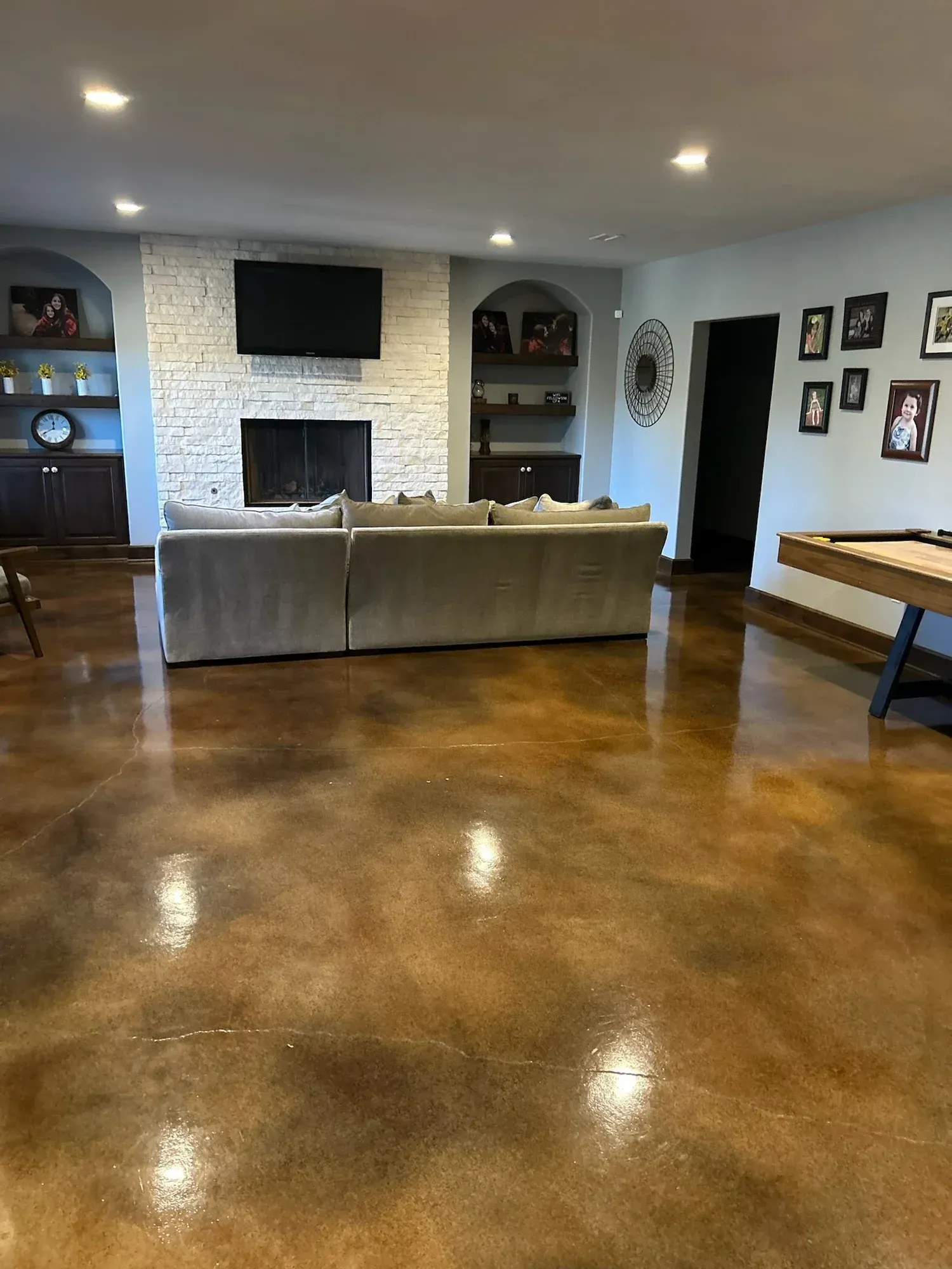 Living room with brown glossy floor, gray sectional sofa, white brick fireplace, recessed lighting, and a pool table.