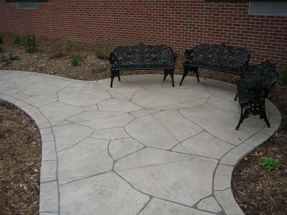 Stone-patterned concrete patio with three black ornate benches in front of a brick building.