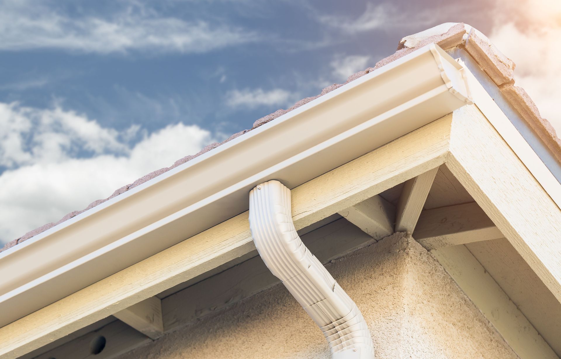 A white gutter on the side of a house with a blue sky in the background.