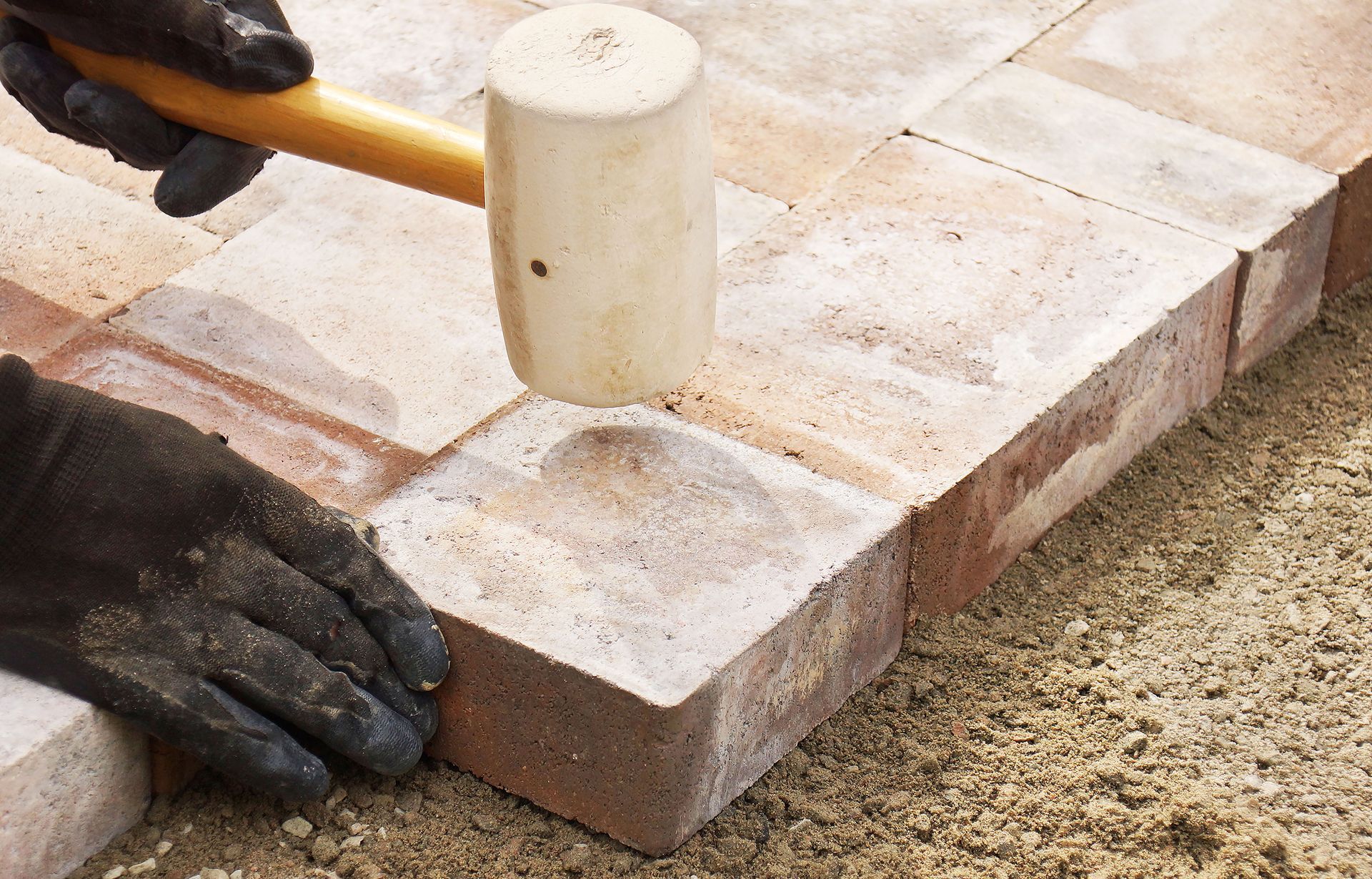 A person is using a rubber mallet to hammer bricks