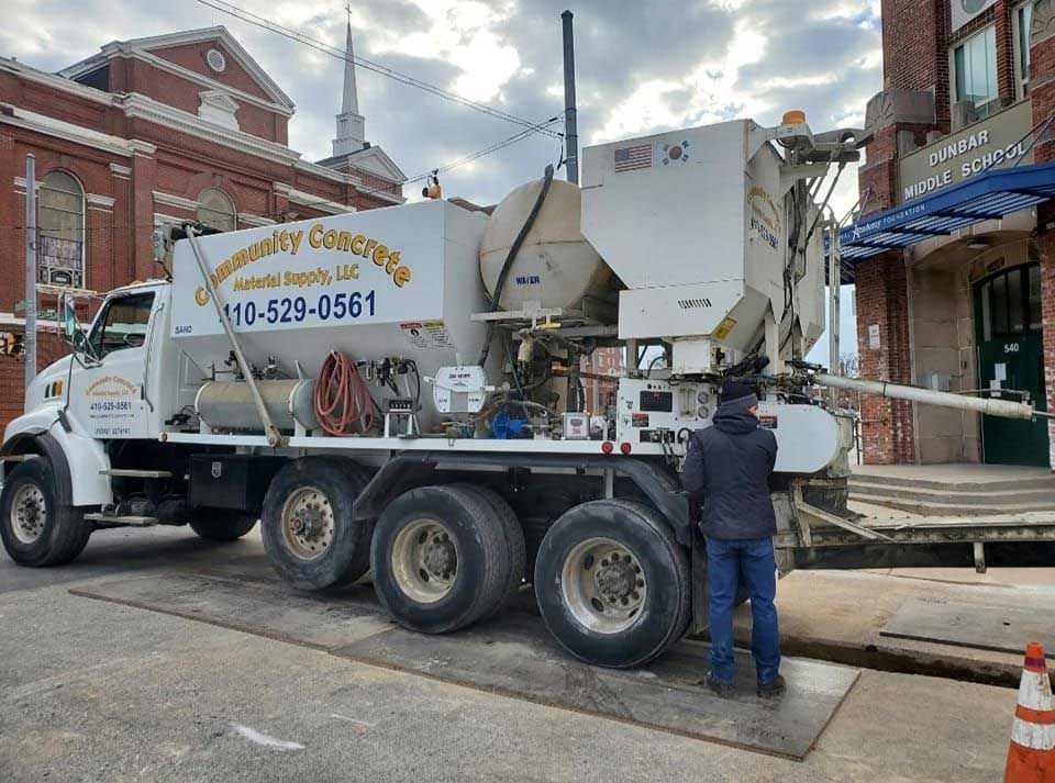 Concrete truck parked on street, worker by the side. Brick building background.