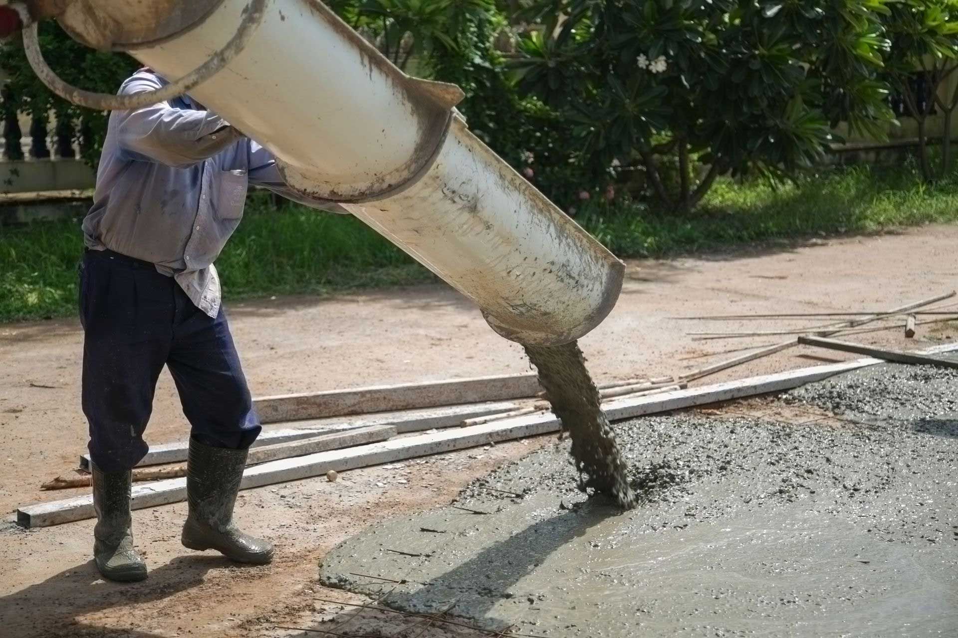 Man pouring wet concrete from a chute onto a prepared surface outdoors.