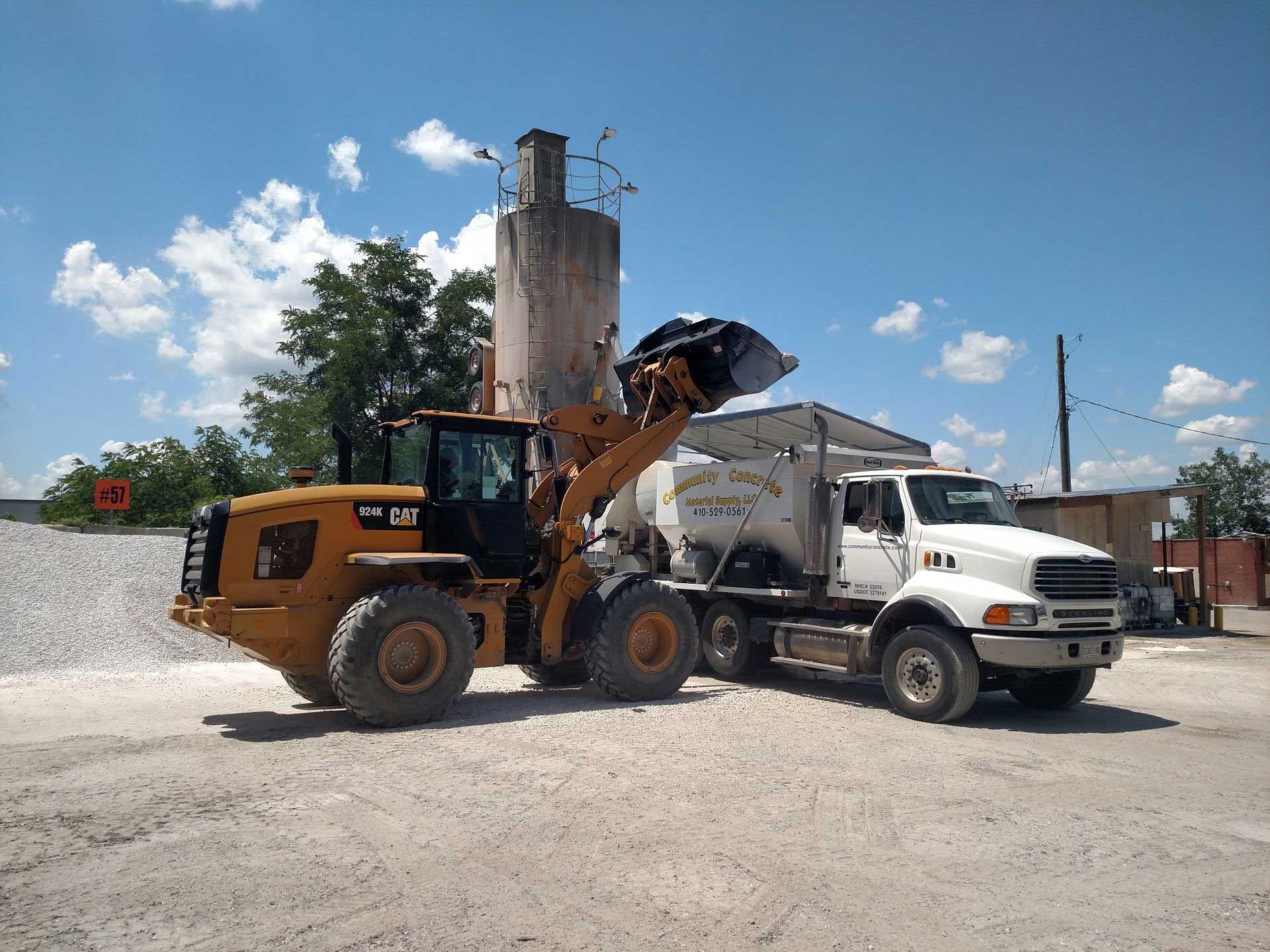 Yellow loader filling white truck with gravel, under a blue sky at a construction site.