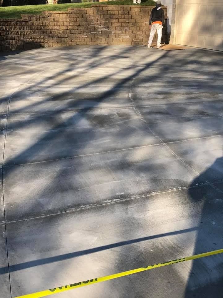 Concrete driveway with long shadows; person standing near wall with caution tape.