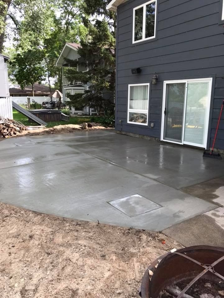 Newly poured concrete patio next to a dark gray house with sliding glass door and windows.