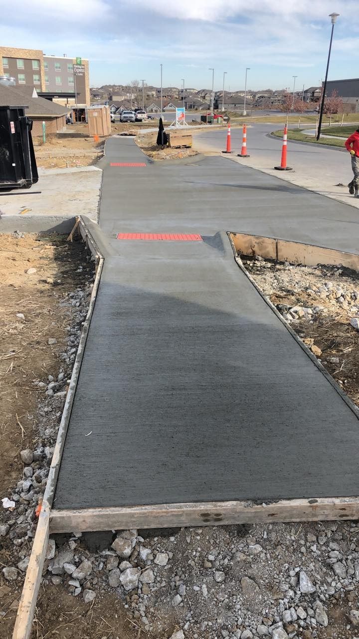 Freshly poured concrete sidewalk under construction, adjacent to a dirt area and street.