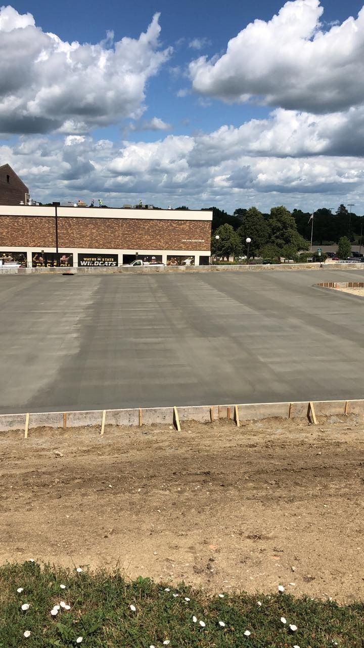 Newly poured concrete parking lot with a brick building and blue sky in the background.