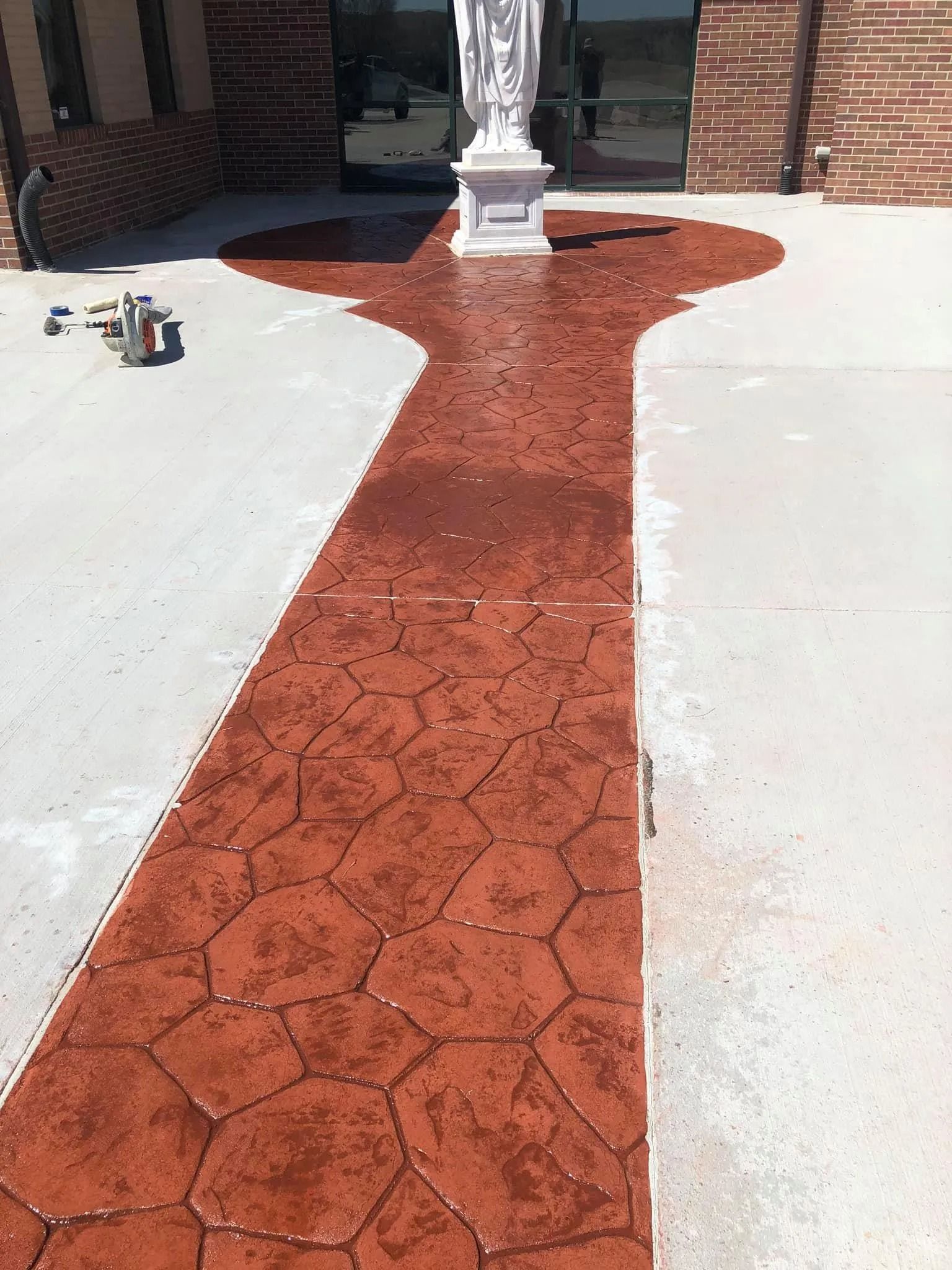 Red stamped concrete walkway leading to a statue in front of a building.