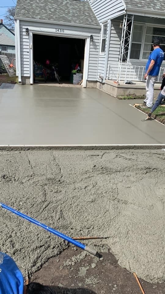 Freshly poured concrete driveway in front of a house, with workers in the background.
