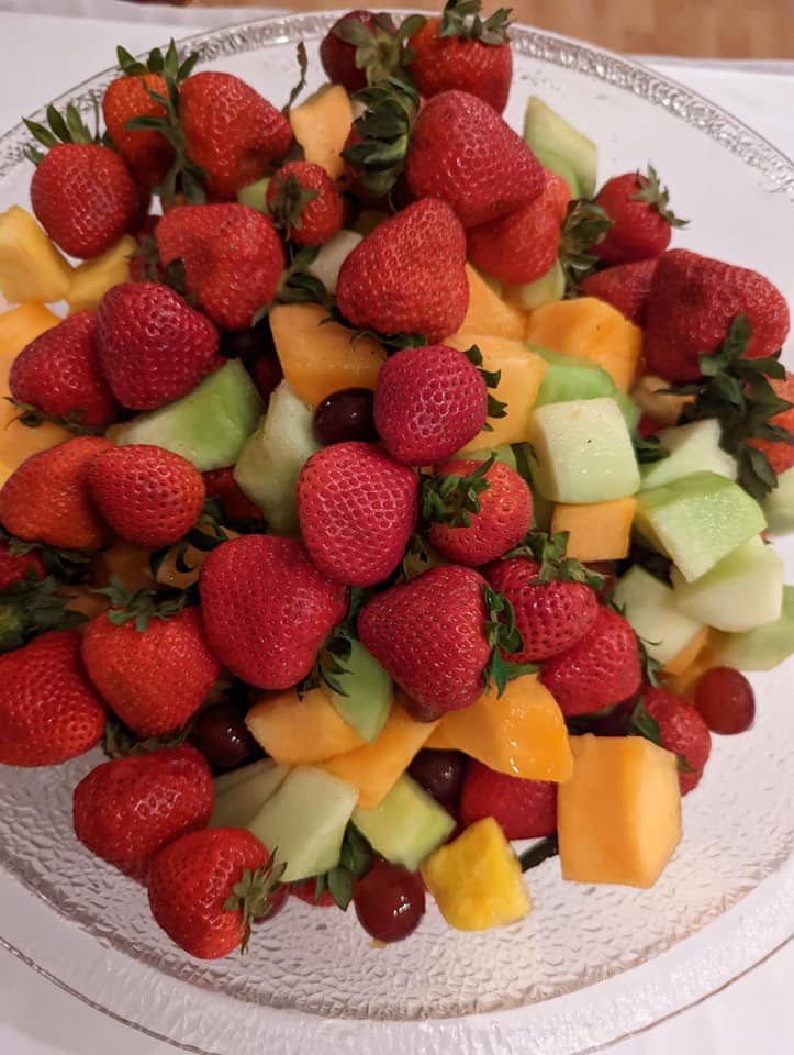 A glass bowl filled with strawberries melon grapes and other fruits