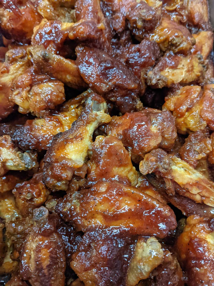A close up of a pile of chicken wings covered in sauce.
