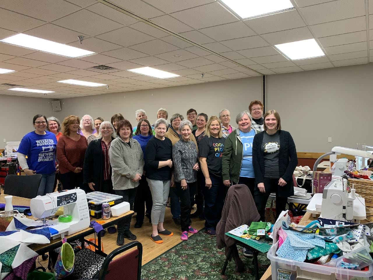 A group of women are posing for a picture in a room filled with sewing machines.