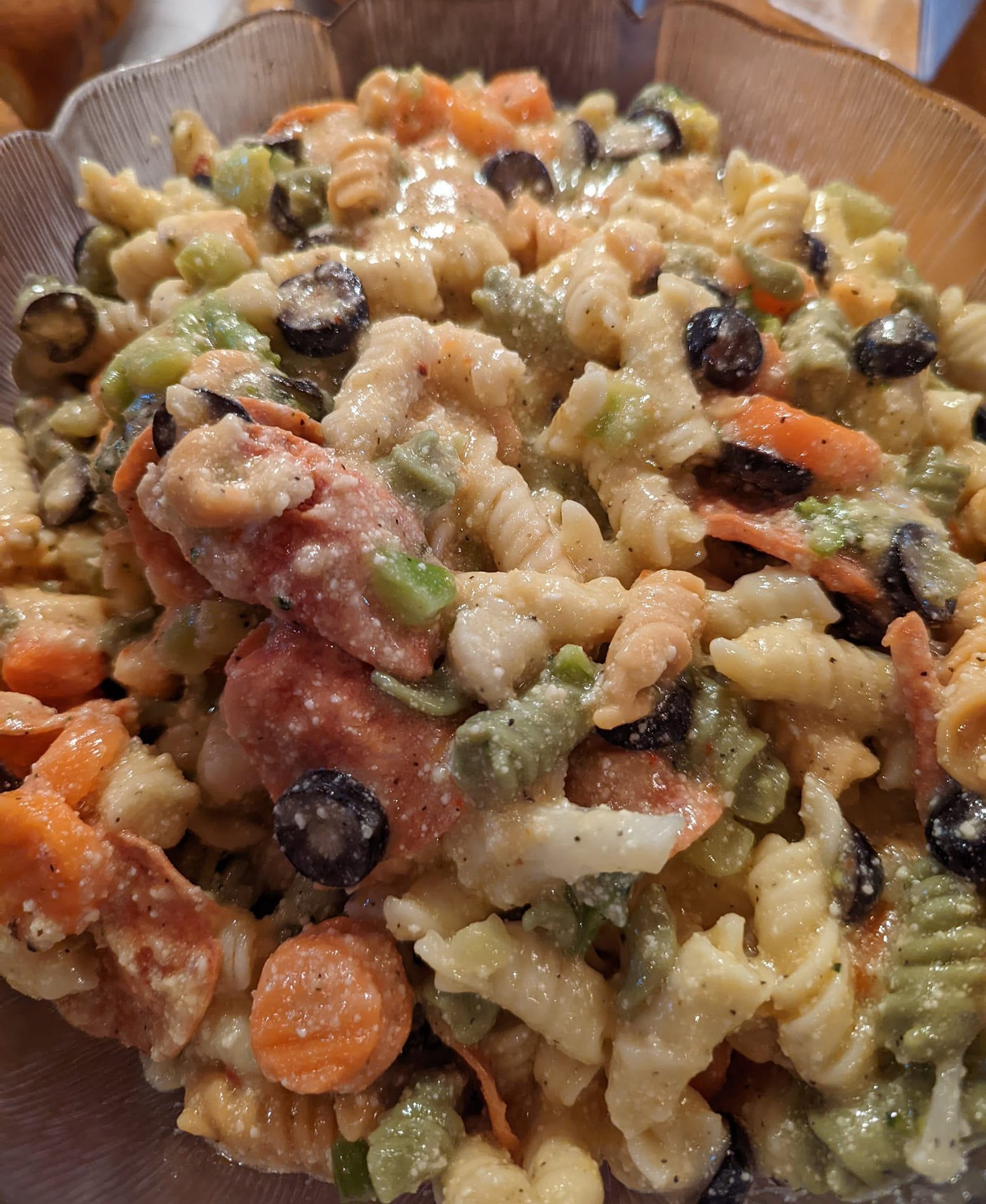 A pasta salad with carrots , celery , olives and bacon in a bowl.