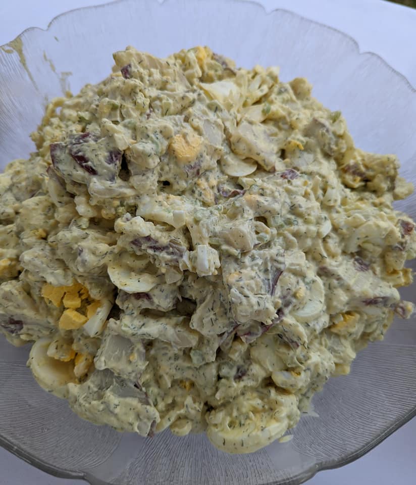 A bowl of potato salad with eggs and onions on a table.