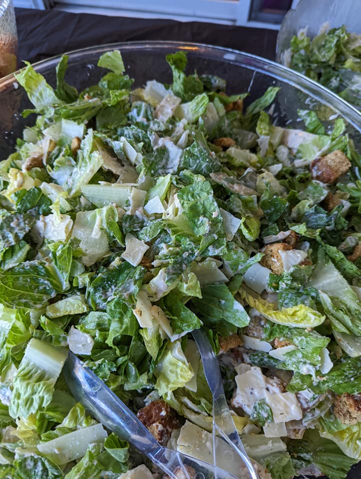 A close up of a caesar salad in a bowl with tongs.