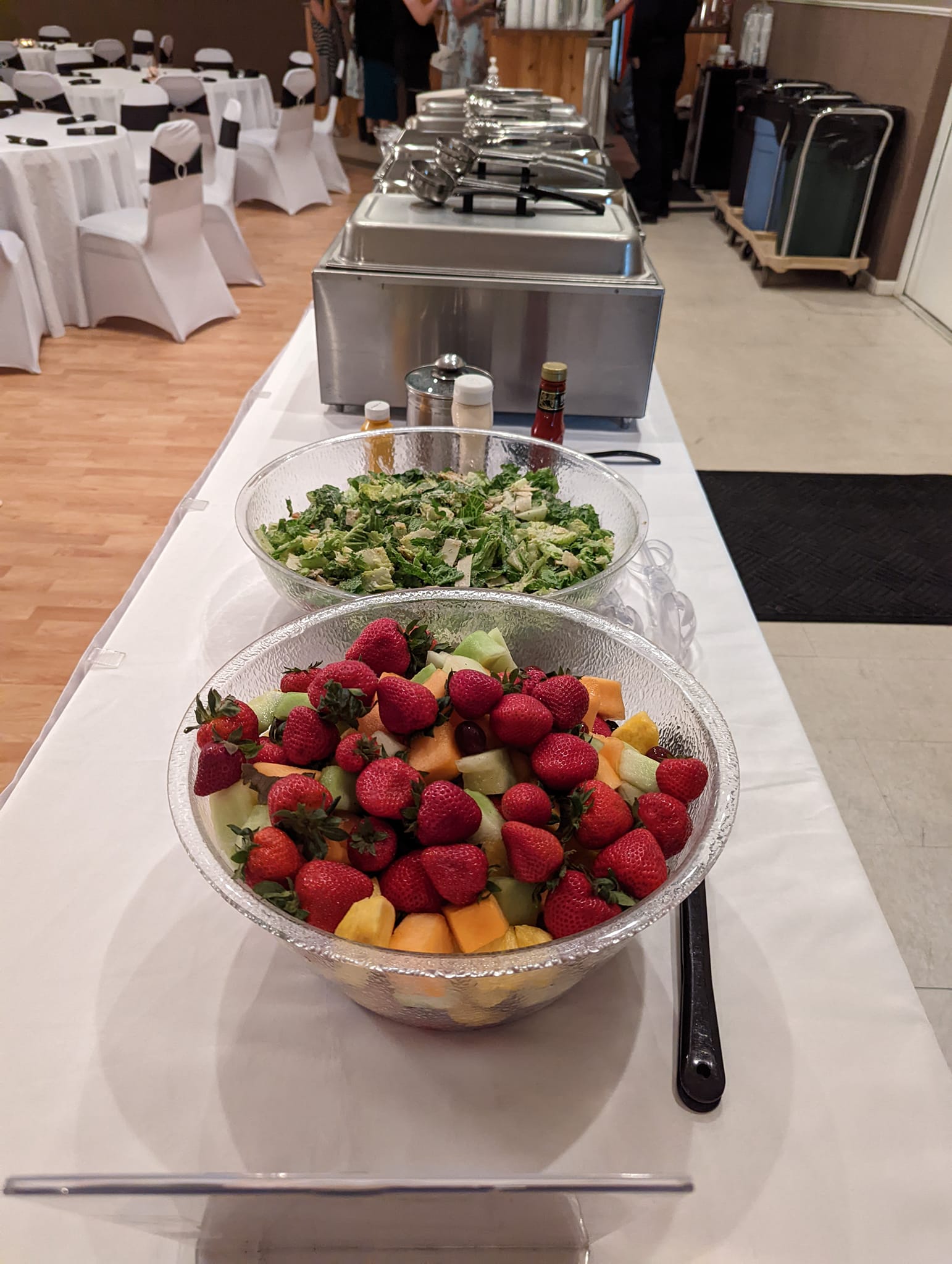 A buffet table with bowls of fruit and salad on it.