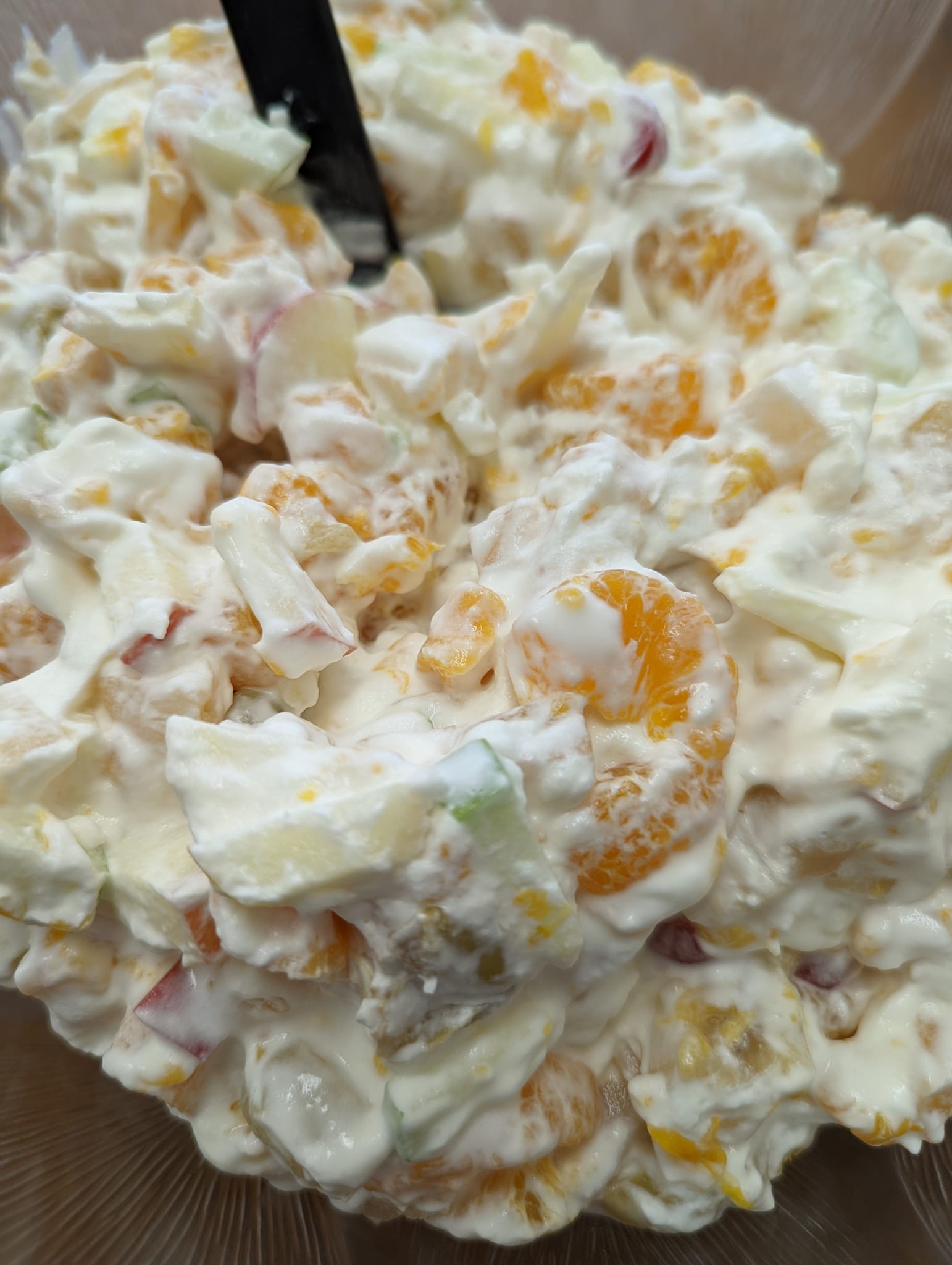 A close up of a bowl of fruit salad with a spoon in it.