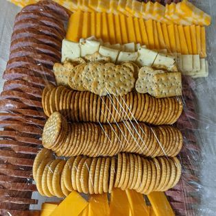 A tray of crackers , cheese , and sausage on a table.