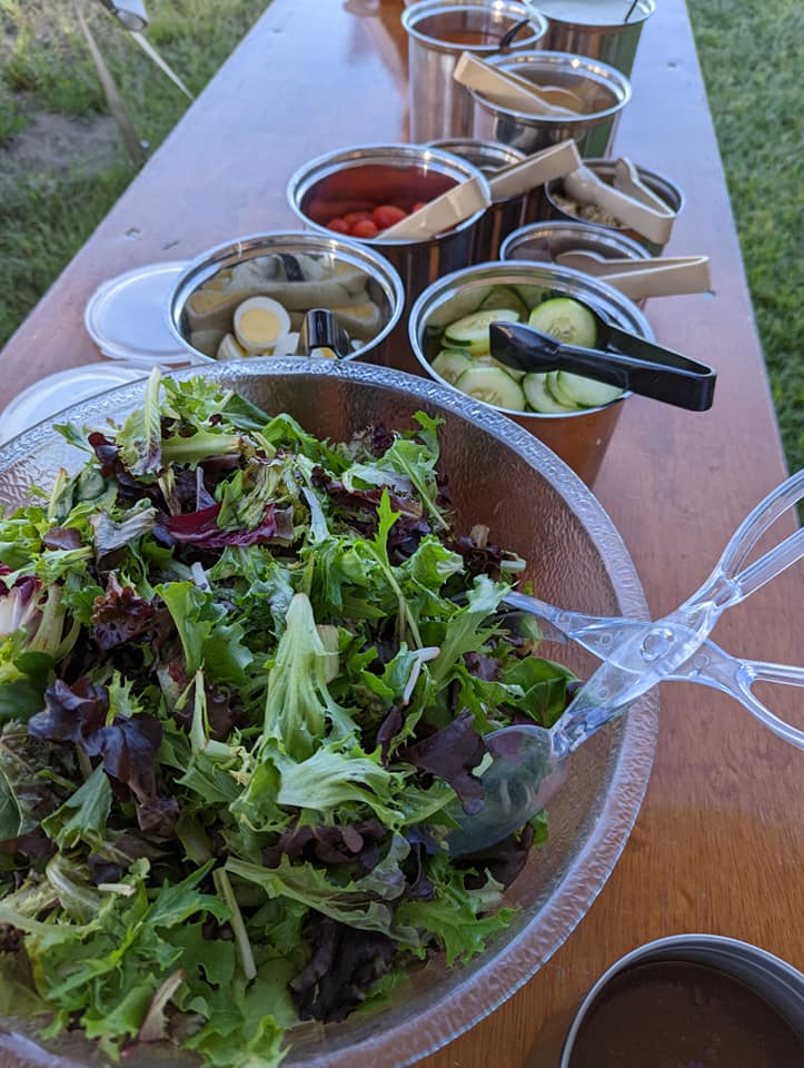 A salad is sitting on a wooden table next to bowls of vegetables and sauces.