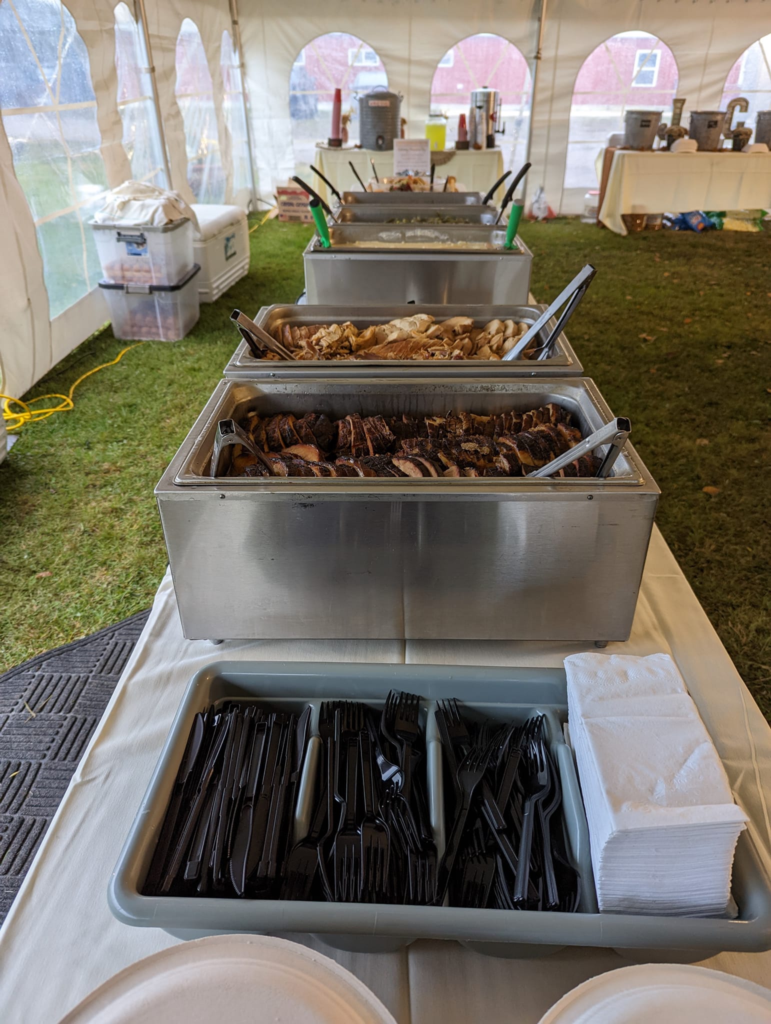 A buffet table with plates , napkins , tongs , and containers of food.